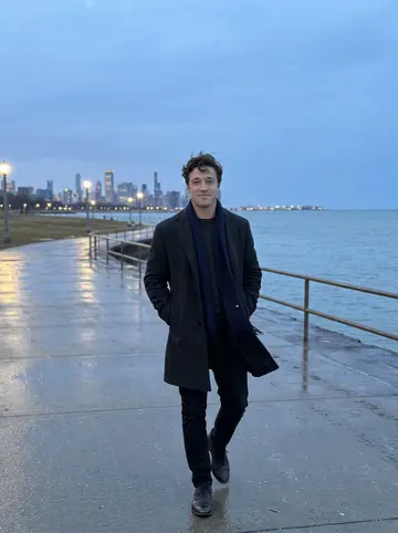 Nenad, AI character: the Lake Michigan shoreline path in March, cold wind off the water and Milwaukee skyline lights far behind