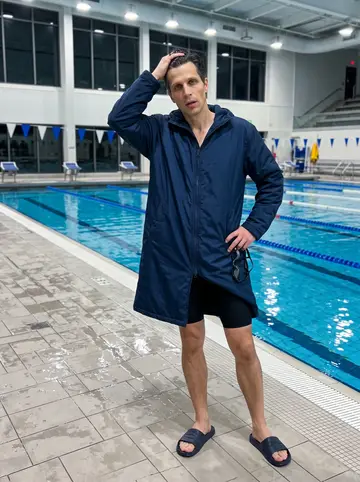 Leonid, AI character: empty university pool deck after midnight, blue lane ropes and still water stretching behind him