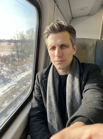 Leonid, AI character: train seat by the window leaving Toronto after visiting family, winter fields sliding past outside