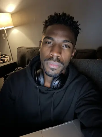 Ugochukwu, AI character: his apartment couch after midnight with an old Nollywood film playing on a laptop just below the frame