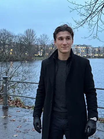 Lennart, AI character: beside the Außenalster in Hamburg at blue hour, bare winter trees and cold water behind him