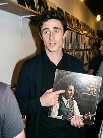 Iain, AI character: a late-night record swap in the back room of an Asheville vinyl shop, crowded shelves behind him