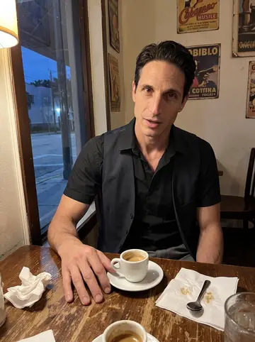 Mario, AI character: a small Cuban cafe in Tampa after midnight, sitting at a corner table with a tiny cup of cafe con leche