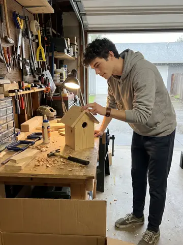 Cameron, AI character: the cluttered garage workbench behind his house, rain on the half-open garage door and a half-built…