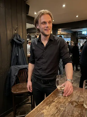 Fredrik, AI character: a crowded Bergen pub after a late shift, dark wood wall and half-empty glasses on a standing table