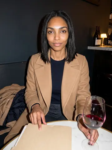 Damilola, AI character: a quiet corner table at a downtown Washington wine bar after a board dinner, coats piled on the bench…