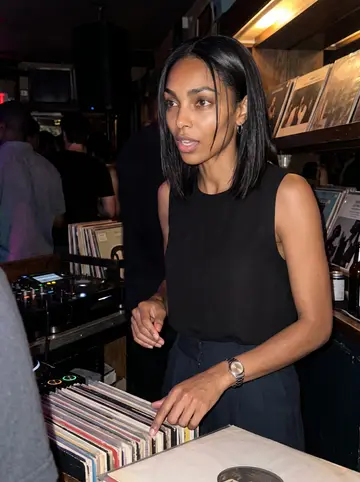Damilola, AI character: a small highlife record night at a low-lit bar in Adams Morgan, vinyl sleeves stacked near the DJ table