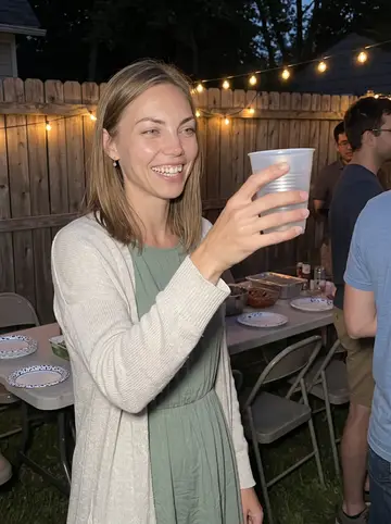 Saskia, AI character: a humid Minneapolis backyard potluck with other grad students, paper plates and string lights behind her