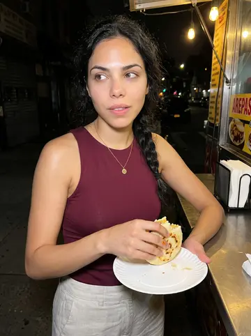 Yurany, AI character: a late-night arepas cart in Jackson Heights, paper plate balanced near the counter