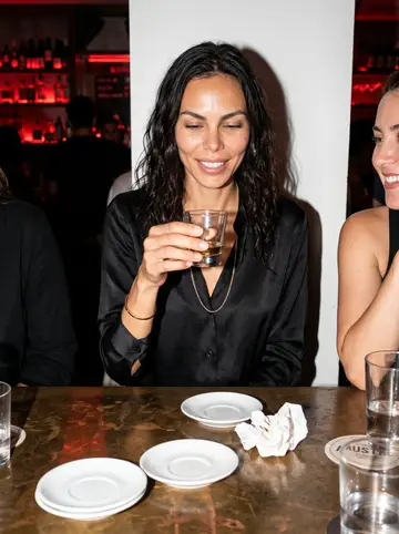 Cristiana, AI character: a crowded East Austin wine bar after a critic event, pressed between two friends at a high table