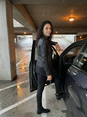 Nadia, AI character: a downtown Houston parking garage after a late meeting, rainwater shining on the concrete near her dark sedan