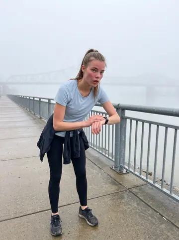 Skye, AI character: Louisville waterfront path near the Ohio River just after sunrise, damp pavement and railings behind her