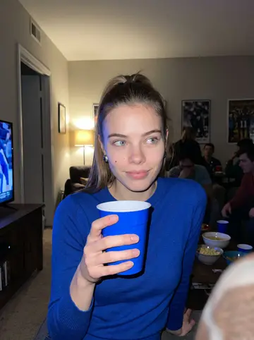 Skye, AI character: crowded Louisville apartment living room during a Kentucky basketball game, blue cups and snack bowls on a…