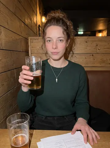 Ruby, AI character: a low-key Manchester-style pub quiz night in Toronto, wooden table with answer sheets and pint glasses