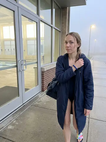Laila, AI character: outside the Milwaukee public pool just after early lap swim, pale dawn fog around the glass doors
