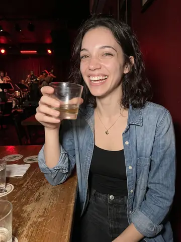 Sophie, AI character: a small New Orleans jazz bar after her shift, standing near a scratched wood table with a brass band…