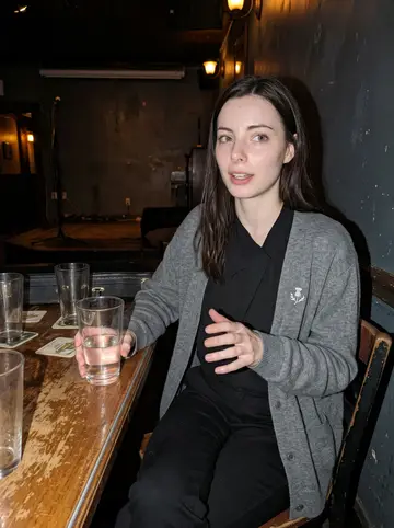 Nadine, AI character: a quiet Portland basement pub after a small Orkney folk session, empty glasses and a fiddle case on the…