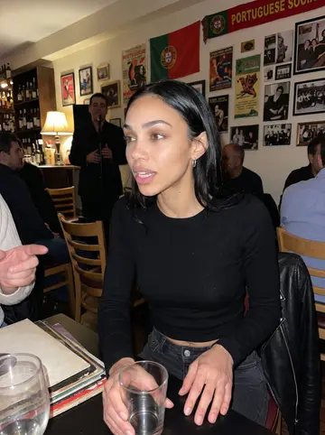 Débora, AI character: small Portuguese social club in Ironbound during a low-key fado night, crowded table with drinks and…
