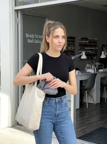 Andrea, AI character: outside the Brady Street nail salon after her shift, glass door and manicure tables behind her, Milwaukee…