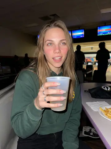 Andrea, AI character: Milwaukee bowling alley during league night, score screens glowing behind her and rented shoes under the table
