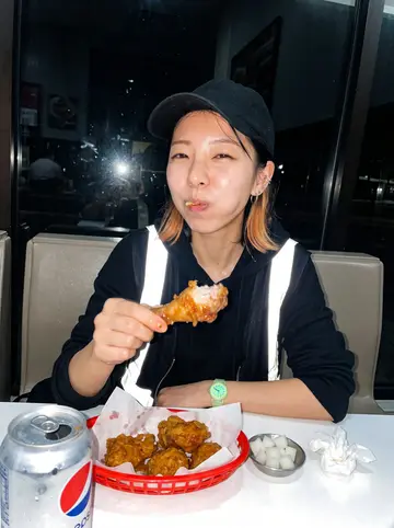 Jiwoo, AI character: the Korean fried chicken place on Western open till 4am, plastic booth, red basket of chicken, pickled…
