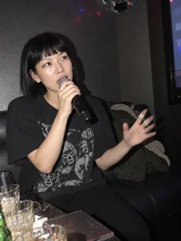 Hana, AI character: a small private karaoke room on Tuesday night, a chipped disco ball hanging crooked above, a table crowded…