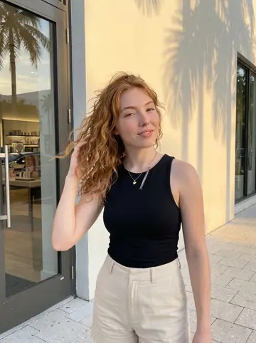 Clarisse, AI character: Miami Design District sidewalk outside a cosmetics store, palm shadows on the pale wall behind her