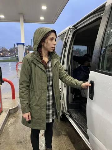 Shauna, AI character: a gas station outside Cleveland at dusk beside the band van after a rainy drive