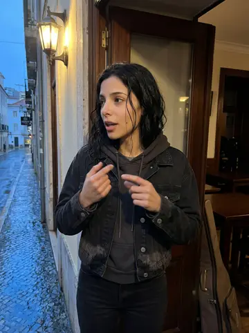 Dolores, AI character: a small fado club in Lisbon after rain, standing near a doorway with dark wood tables and a singer's…