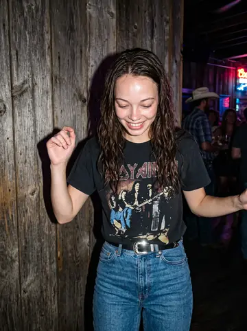 Jade, AI character: a crowded Nashville line-dancing bar, pressed near a wood wall and neon-colored stage lights after she…