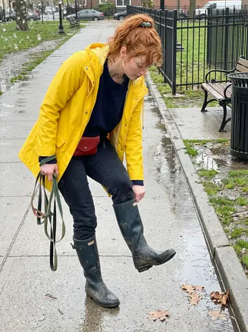 Jodie, AI character: wet sidewalk by a small neighborhood park in Philadelphia, empty leads looped over one wrist after a…