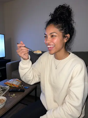 Sarah, AI character: her apartment living room during a low-key baking show night with her roommate, blankets and cereal bowls…