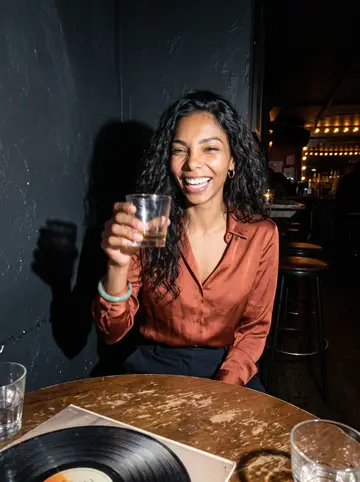 Tamara, AI character: small neighborhood jazz bar after dinner service, round table with a record sleeve and low drinks