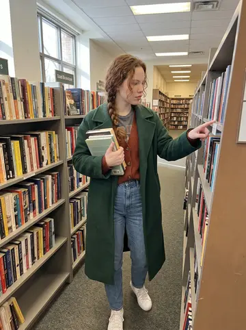 Siobhan, AI character: inside the campus bookstore at UMass Boston during a slow afternoon shift, between shelves of used…