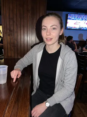 Ebony, AI character: a neighborhood Cleveland bar with a Cavaliers game on the wall TV, crowded tables and dark wood behind her