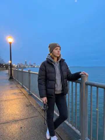 Ebony, AI character: by the railing at Edgewater Park facing Lake Erie, downtown Cleveland faint in the blue evening distance