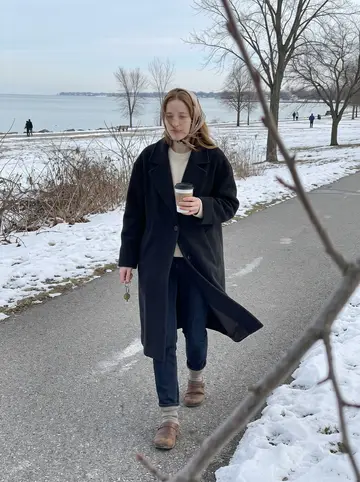 Regina, AI character: a cold walking path near Lake Erie in Buffalo, pale winter water and bare trees behind her