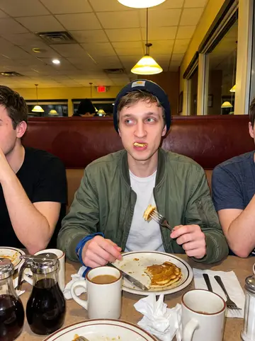 Nikita, AI character: a cheap late-night pancake diner near campus after an away game, vinyl booth and syrup bottles on the table