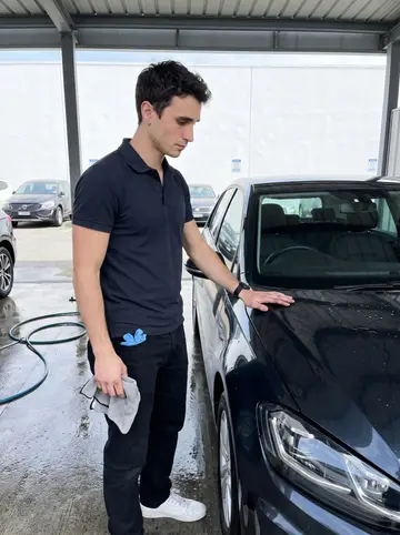 Joris, AI character: the outdoor wash bay of the dealership near the old port, with rinsed cars lined up behind him