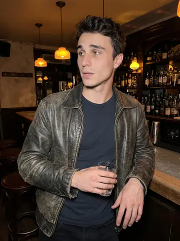 Joris, AI character: a small crowded bar near the old port after closing time at the dealership, standing near the counter with…
