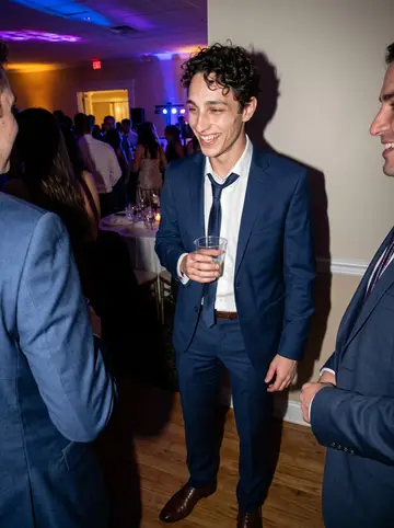 Enrico, AI character: his cousin Gina's June wedding reception in a North Shore banquet hall, dance floor crowded behind him