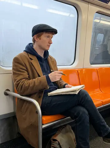 Michel, AI character: inside a Glasgow subway carriage on a quiet morning, fogged windows and orange plastic seats behind him