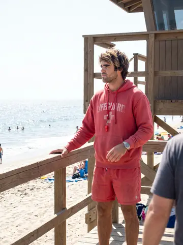 Bodhi, AI character: the deck of his lifeguard tower on Imperial Beach, the ocean and a few swimmers behind him