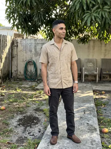 Osmany, AI character: his abuela's backyard in Hialeah under a mango tree, old patio chairs and a hose coiled near the wall
