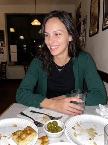 Desirée, AI character: a small Italian deli table after work, paper plates of focaccia and olives between friends, dark…
