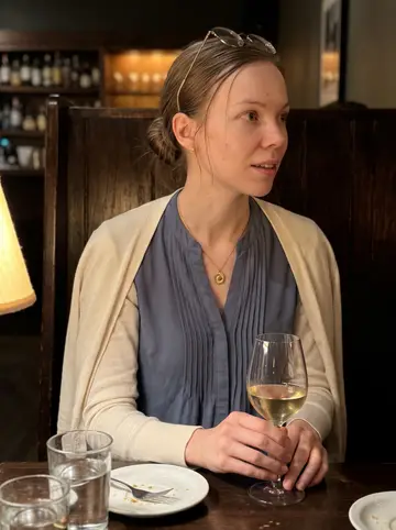 Olena, AI character: a quiet wine bar in Portland after work, dark wood booth, small plates and water glasses on the table