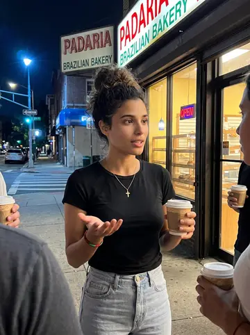 Aline, AI character: sidewalk outside a Newark Brazilian bakery after rehearsal, humid night, friends half-cropped around her…