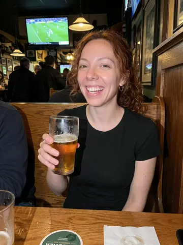 Yvonne, AI character: inside a small Irish pub in Tampa during a Sunday hurling match, crowded wooden booth and TV glow behind her