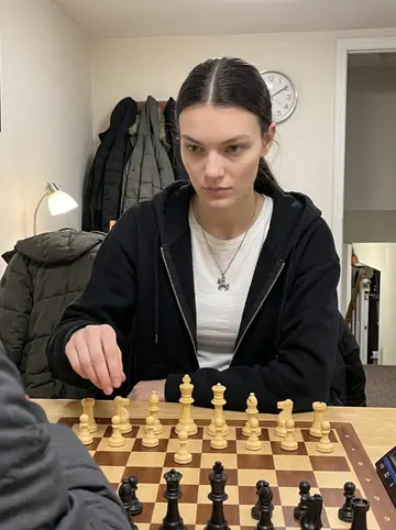 Yaroslava, AI character: a cramped Baltimore chess club room above a small shop, winter coats on chair backs, analogue clock on the…