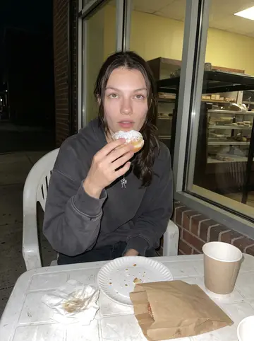 Yaroslava, AI character: outside a corner pastry shop in Baltimore after a late shift, plastic table near the window